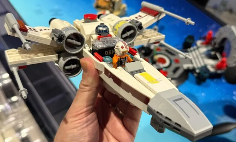 Hand holds a Lego X-Wing fighter with pilot and R2-D2.