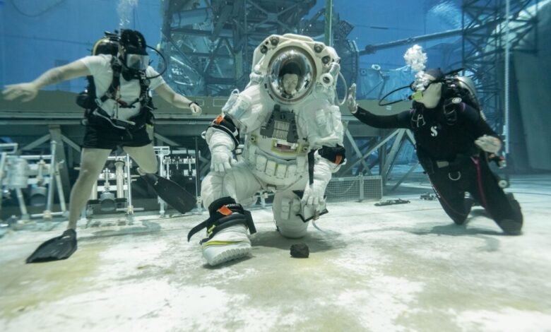 Astronaut in spacesuit kneels underwater with divers during NBL integration testing.
