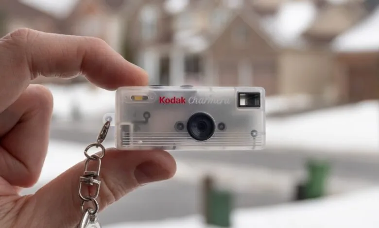 Hand holds a Kodak Charmera camera keychain against a blurred outdoor background.