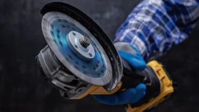 Angle grinder in motion, held by gloved hand, blue plaid shirt.