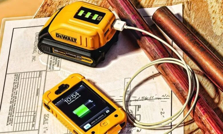 Yellow DeWalt battery charging a phone on top of engineering plans.