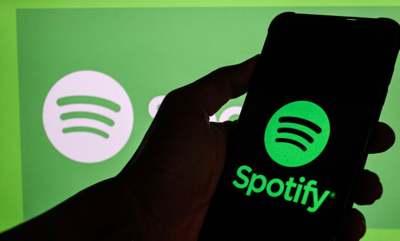 Hand holding phone displaying the Spotify logo against a green background.