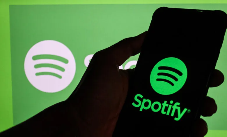 Hand holding phone displaying the Spotify logo against a green background.