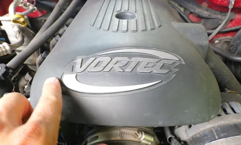 Close-up of a Vortec engine cover with a finger pointing at it.