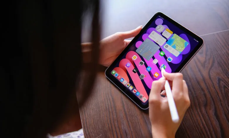 Person using Apple Pencil on iPad Mini with widgets displayed.