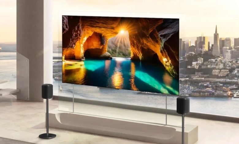 Transparent TV displays cave scene with city view behind, speakers on stands.