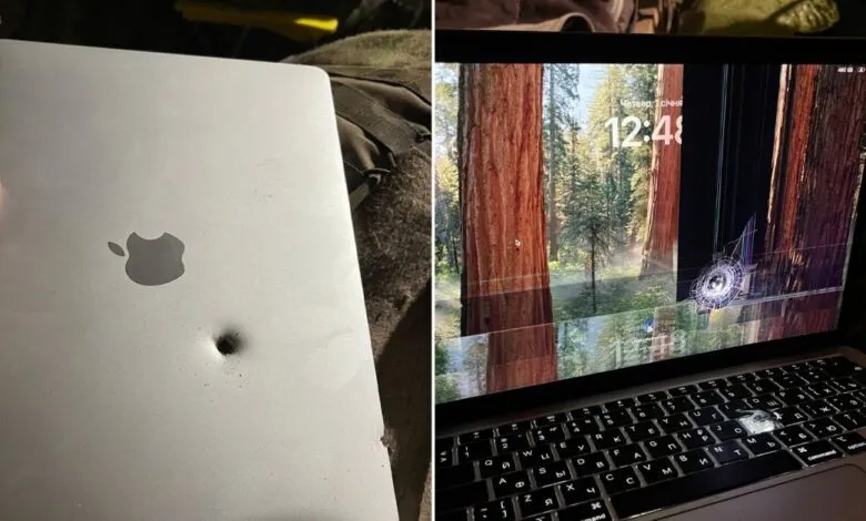 Damaged MacBook Air with bullet hole and shattered screen showing forest background.