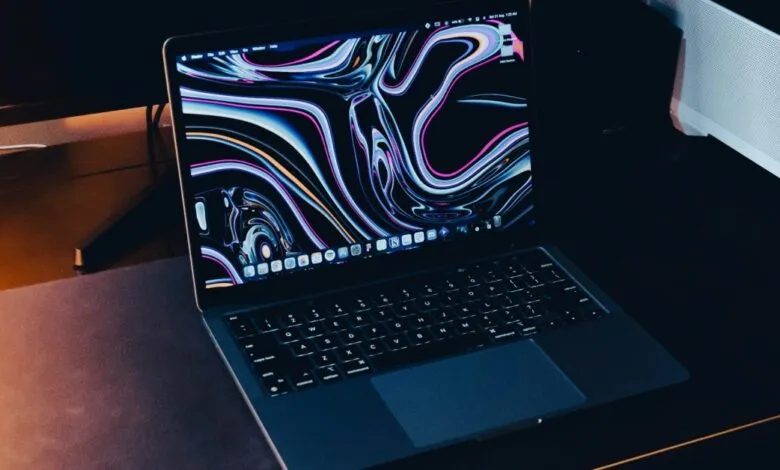 MacBook Pro on desk with colorful abstract wallpaper on screen.