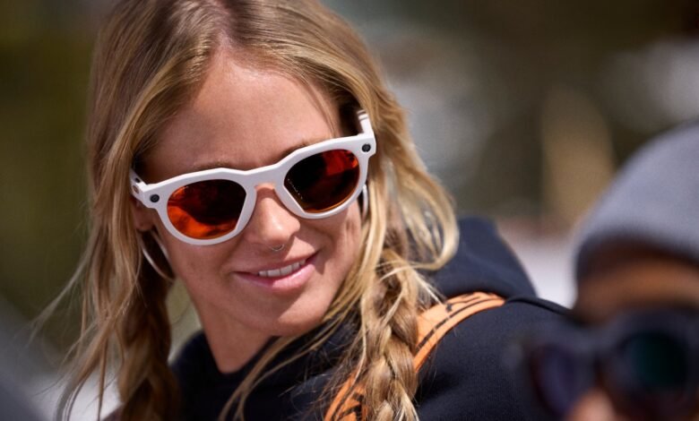 Woman with blonde braids wearing white Oakley sunglasses smiles outdoors.