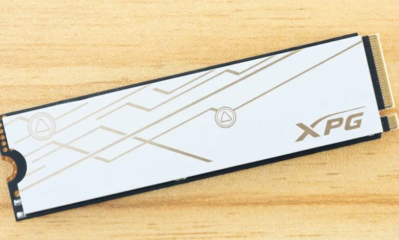XPG M.2 NVMe SSD with white heatsink and gold accents on wood surface.
