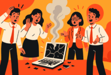 Four people react to a smoking, broken laptop on a desk.