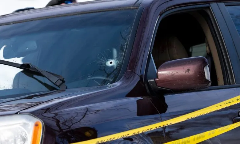 Car windshield with bullet hole, surrounded by police tape.