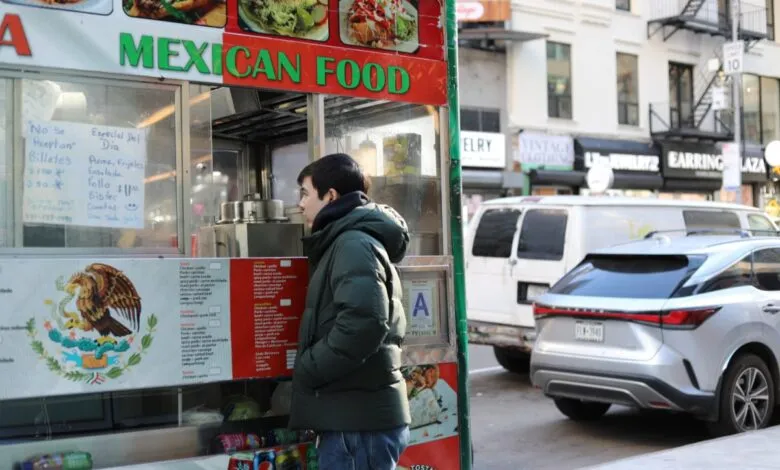 Person stands at a Mexican food cart on a city street.