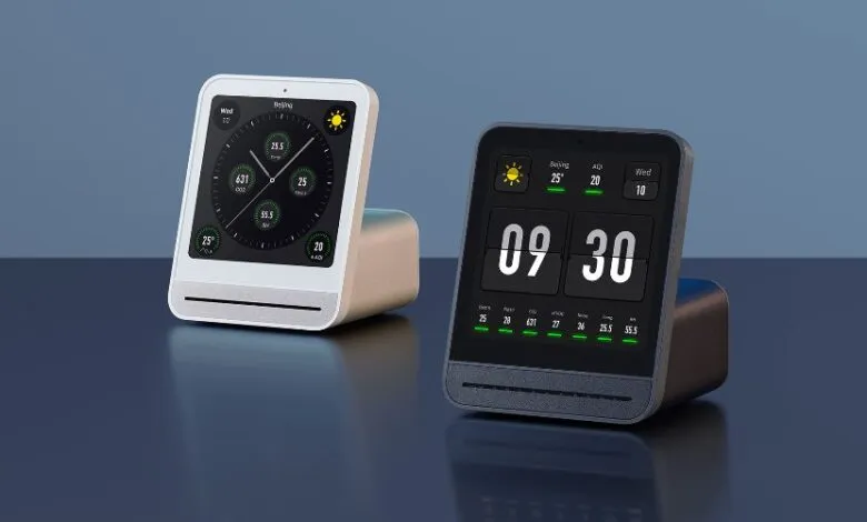 Two Qingping air quality monitors, one white and one black, display time and air quality data.