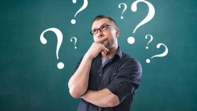 Man with glasses thinking surrounded by question marks.