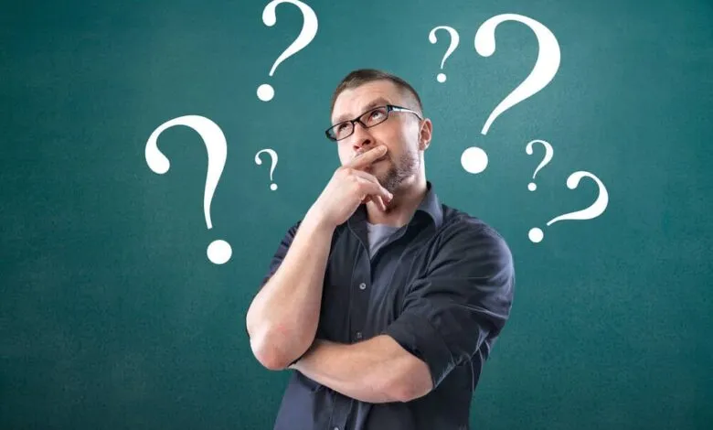 Man with glasses thinking surrounded by question marks.