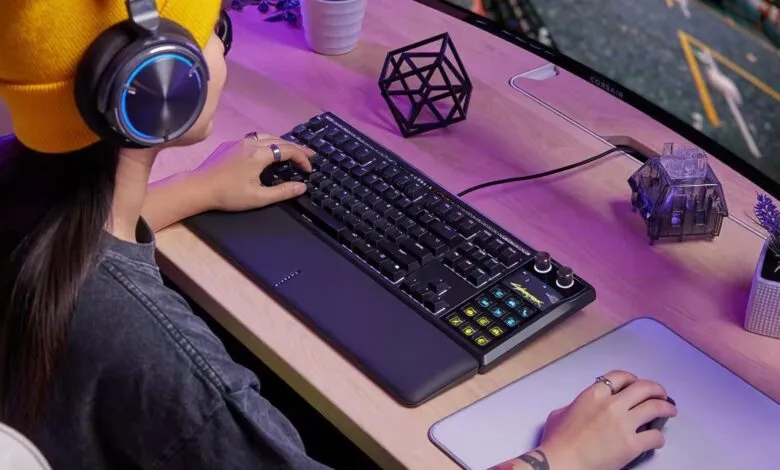 Person using Corsair gaming keyboard with headphones on desk.