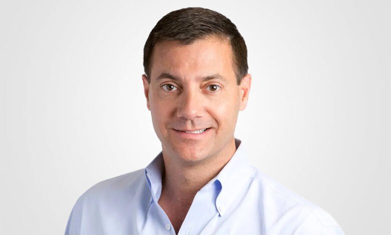 Headshot of a man with short dark hair and a light blue shirt.