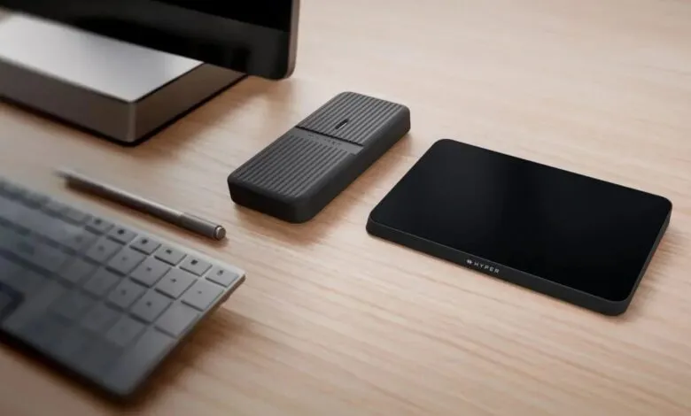 Desk setup with keyboard, pen, charger, and Hyper device on a wooden surface.
