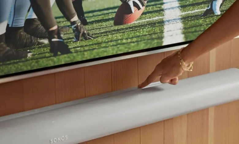 Person touches Sonos soundbar below TV showing football game.