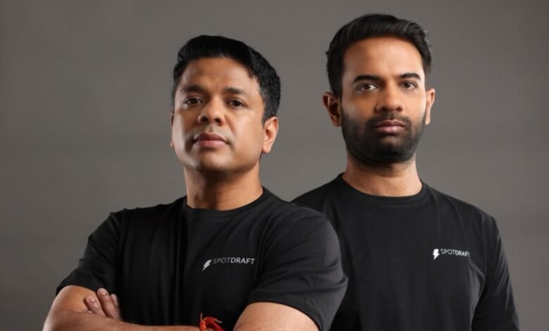 Two men in black SpotDraft shirts stand against a gray backdrop.