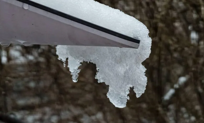Snow and icicles hang from a gray roof edge, water droplets visible.