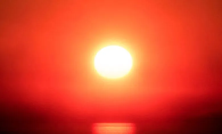 Bright sun over water with red sky and horizon.