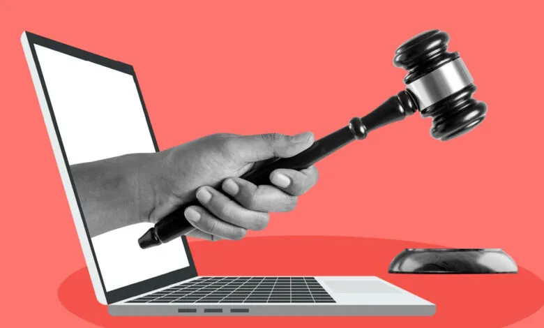 Hand emerges from laptop holding gavel against a red background.