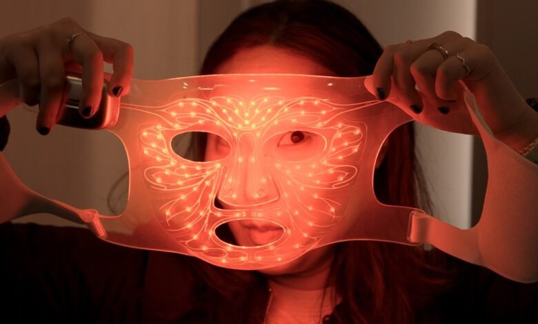 Person holding up a glowing LED face mask with red lights.