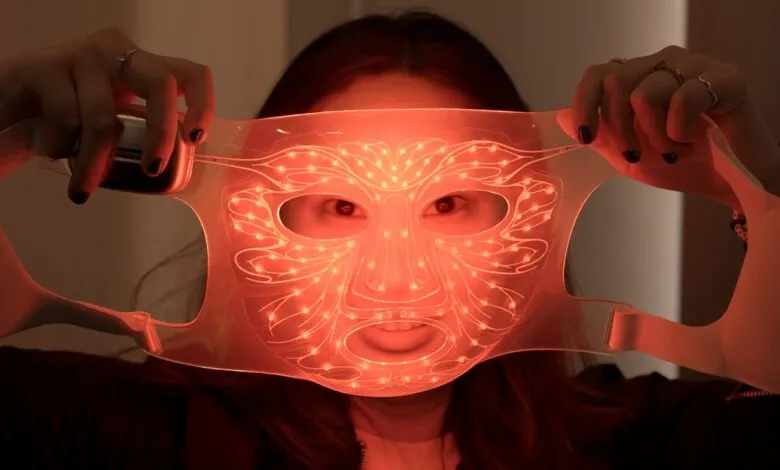 Person holding up a glowing red LED face mask, eyes visible through openings.