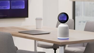 Smart speaker with round screen on conference table in modern office setting.