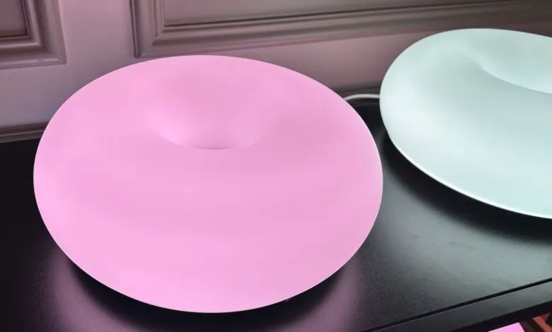 Two donut-shaped lamps, one pink and one light green, on a black surface.