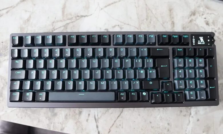 Black mechanical keyboard with teal backlight on a marble surface.