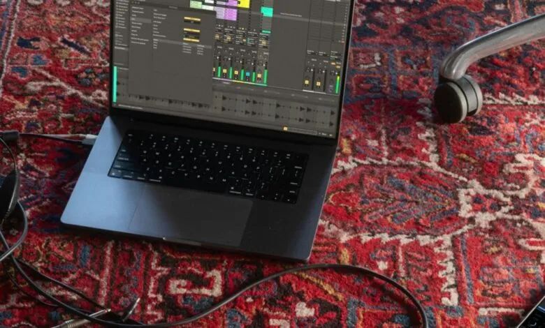 Laptop displaying music production software on a red patterned rug.
