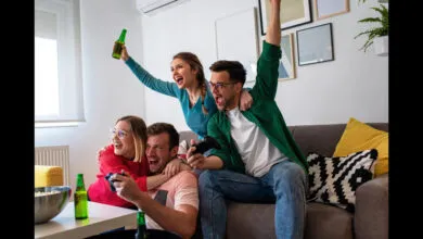 Four friends celebrate while playing video games, holding controllers and beers.
