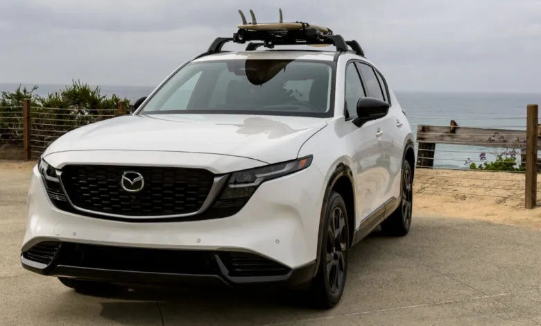 White Mazda CX-5 SUV parked near the ocean with surfboards on the roof rack.