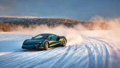 Teal McLaren sports car drifting on a snowy track with snow spraying behind it.