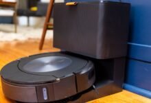 Black Roomba robot vacuum docked at its charging station on hardwood floor.