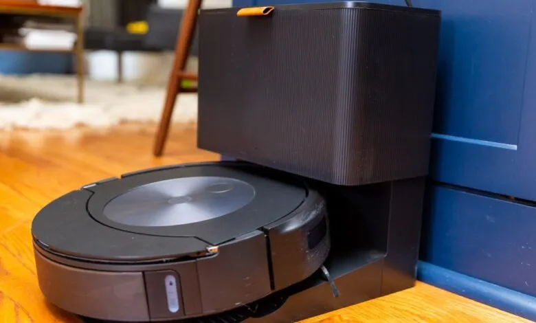 Black Roomba robot vacuum docked at its charging station on hardwood floor.