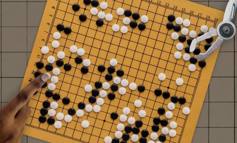 Go board with black and white stones, played by human and robotic hands.