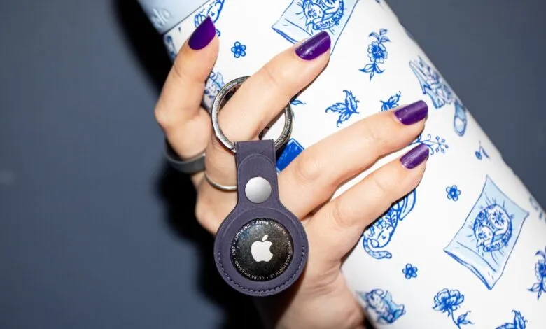 Hand holding Apple AirTag attached to a patterned water bottle.