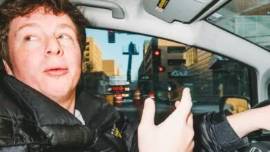 Man driving car, looking left with city street view through window.