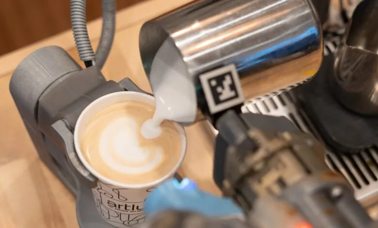 Robot arm pouring milk into a cup of coffee, creating latte art.
