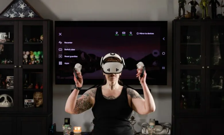 Woman with tattoos wearing VR headset and holding controllers in living room.