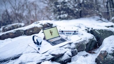 Asus ROG Flow Z13 tablet, headphones, mouse, and case on snowy rocks.