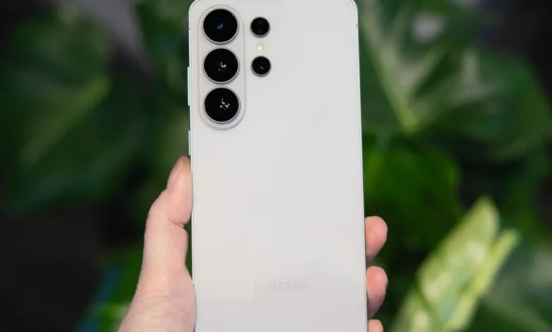 Hand holding a white Samsung Galaxy phone showing the camera array.