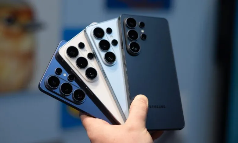 Hand holds four Samsung Galaxy phones in blue, white, and dark blue colors.