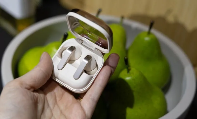 Hand holds open earbuds case with pears in background.