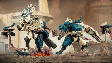 Two Tau battlesuits stand ready with drones in a desert landscape.