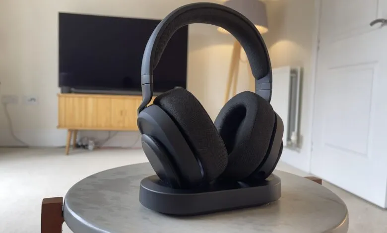 Black wireless headphones resting on a charging dock in a modern living room.